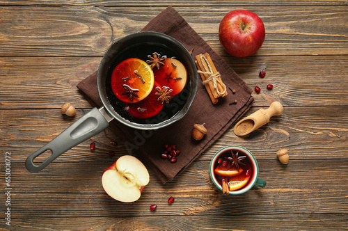 Saucepan and cup of hot mulled wine with orange on wooden background