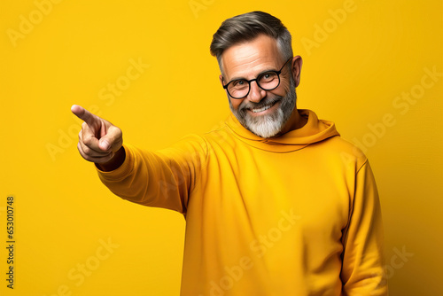 middle age man wearing yellow casual clothes pointing with finger and hand to the side looking at the camera against a yellow background