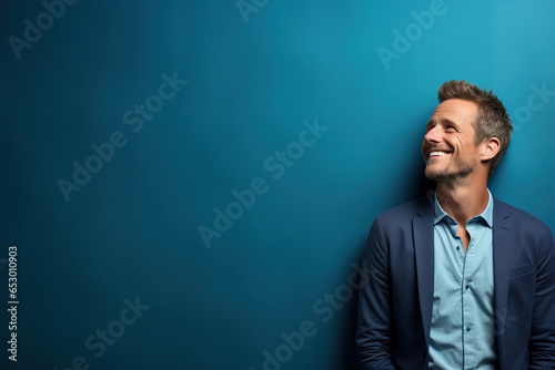 young handsome man wearing formal clothes looking up and to the side against a blue background with copy space