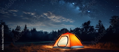 Moonlit campsite beneath starry sky with orange tent in beautiful natural setting