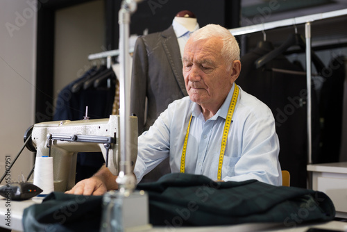 Portrait of elderly man tailor working on sewing machine at studio