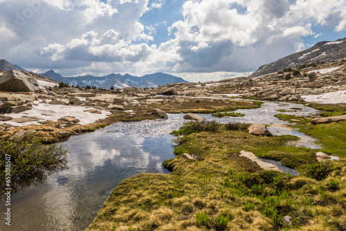 Creek with grassy shore and reflected clouds in the high mountains
