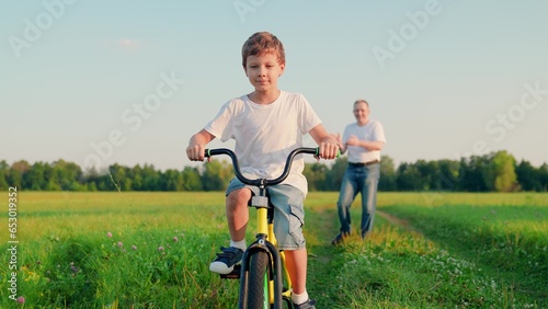 Father teaches his son child to ride bicycle in park. Child is learning to ride bike. Happy family, son dad. Child rides bicycle for first time. Boy kid dream of traveling by bike. Dad helps child.