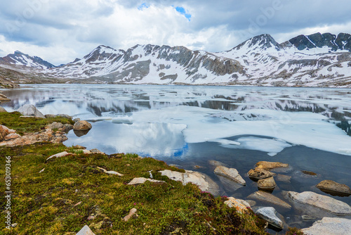Ice floating on high altitude lake surrounded by snow covered mountains and green grass shore in the Eastern Sierras