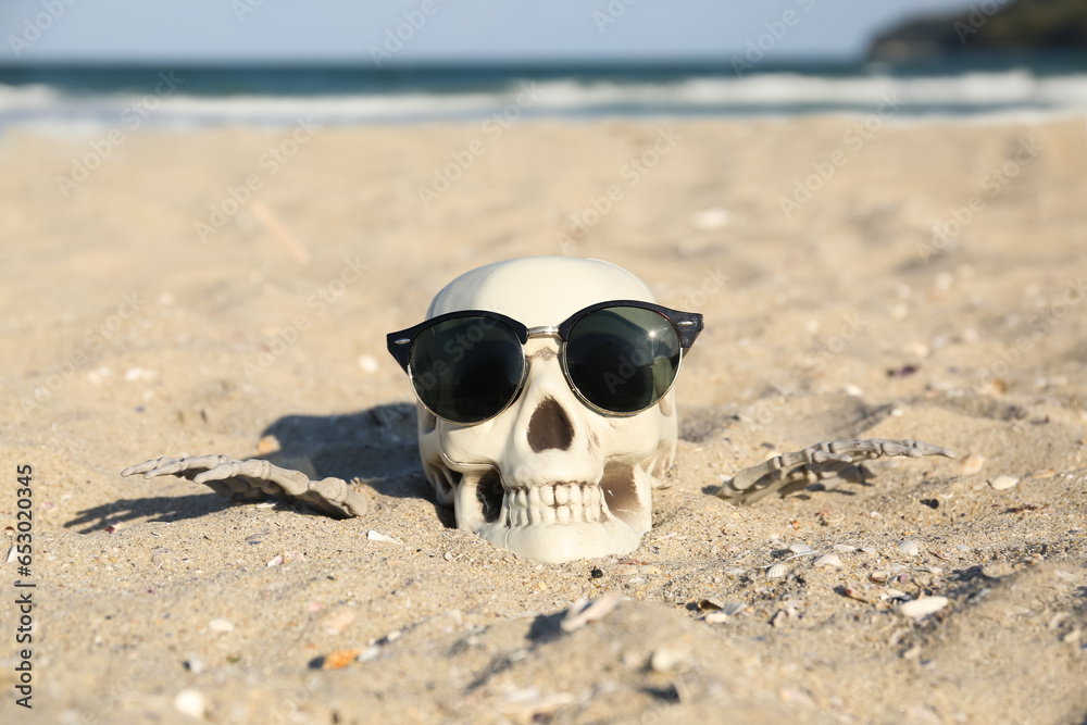 Skull for Halloween with stylish sunglasses and skeleton hands on beach