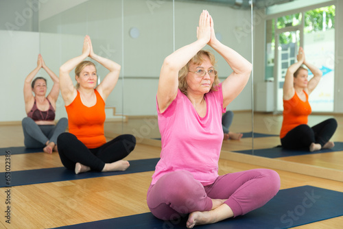 Mature European women are exercising lotus pose in fitness room