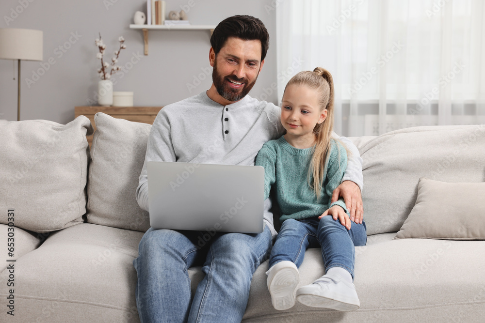 Happy man and his daughter with laptop on sofa at home