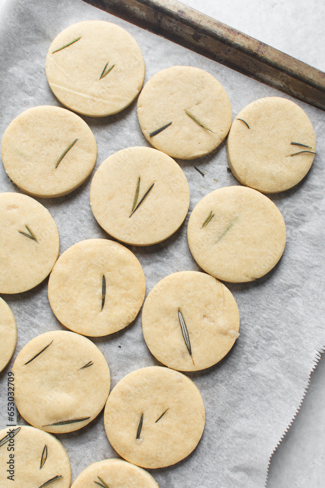 Top view of rosemary sugar cookies on a parchment lined baking sheet, baked rosemary cookie on a white background, process of making rosemary sugar cookies
