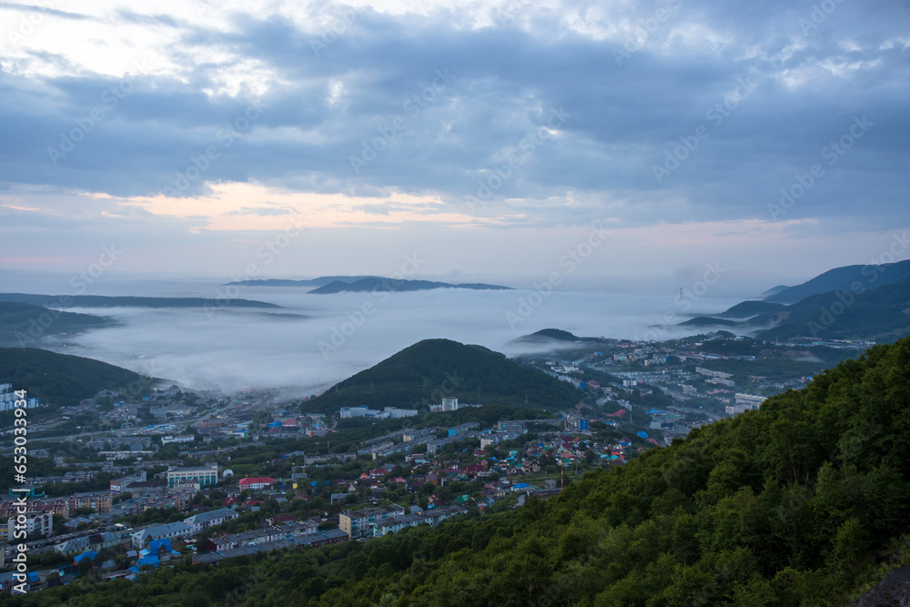 Morning misty landscape. Top view of the city and surroundings. Fog and low clouds over the city and hills. Residential urban areas at dawn. Petropavlovsk-Kamchatsky, Kamchatka, Far East of Russia.