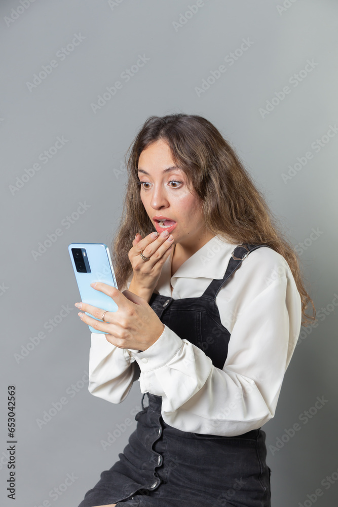 Young Woman Worried about News on her Smartphone: Hand on Mouth Smartphone and Vintage Clothing, Portrait of Woman with Smartphone and Retro Style Clothing Vertical Young Woman Worried about News on her Smartphone: Hand on Mouth Smartphone and Vintage Clothing, Portrait of Woman with Smartphone and Retro Style Clothing Vertical