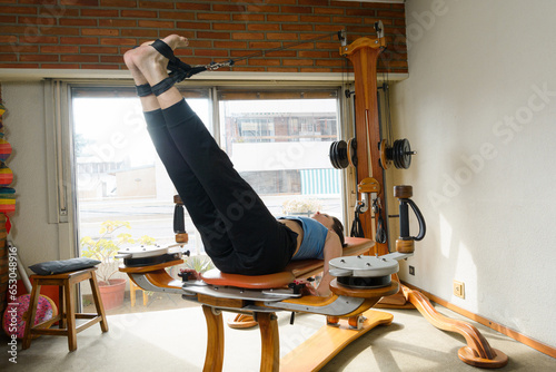 Caucasian woman lying on back on exercise machine with pulleys and weights, legs extended upwards photo