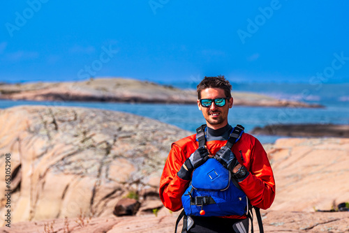 sea kayaking safety equipment: sea kayaker on a rocky shore wearing drysuit pfd sunglasses and paddling gloves photo