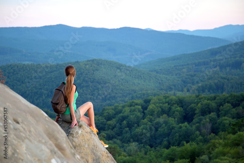 Tired hiker girl relaxing on rocky mountain top enjoying evening nature during travelling on wilderness trail. Lonely woman traveler traversing high hilltop route. Healthy lifestyle concept