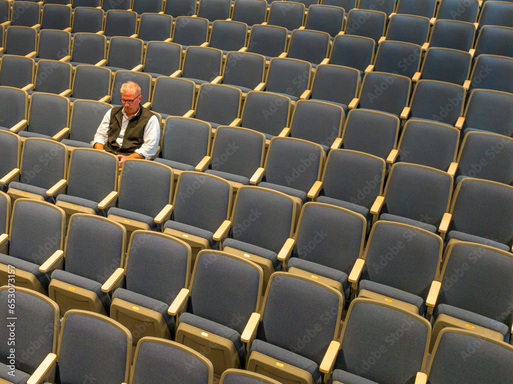 Naklejka premium Overhead view a middle age man with gray hair sitting alone in an empty, auditorium seats, chairs.