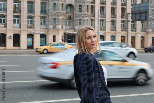 Confident young female executive outdoor half-turned near the road. Blurred background of passing cars.