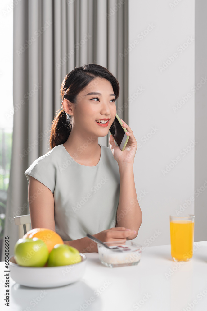 Attractive smiling young woman having a healthy breakfast and talking on mobile phone Attractive smiling young woman having a healthy breakfast and talking on mobile phone