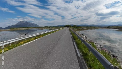 View of the Helgeland coast near Trjøtta in Norway. Hyperlapse cycling the bike on the way to Seven sisters mountain range. Water reflection on the both sides of the road photo