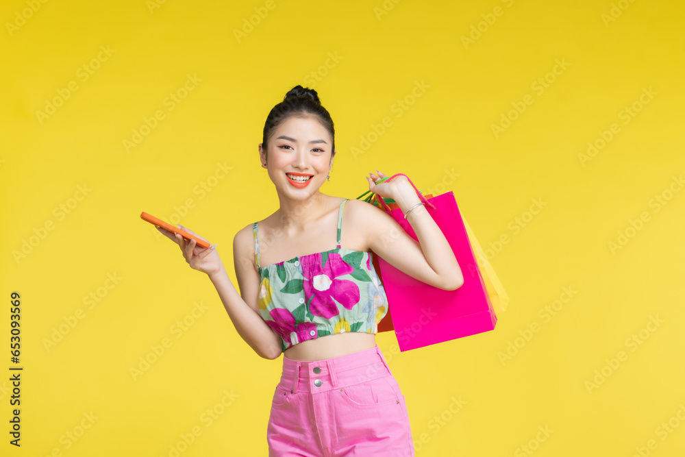 Confident fashionable young Asian woman in sexy dress holding colorful shopping bags and smartphone Confident fashionable young Asian woman in sexy dress holding colorful shopping bags and smartphone