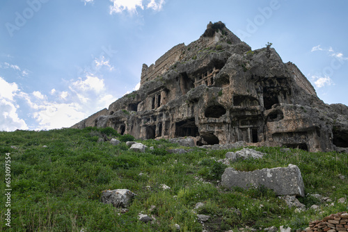 Gray rock-cut ancient ruins and ruined dead city: carved windows, passages, doors, arches. Remains of ancient Lycia civilization, Tlos antique city in Turkey.  Mountain landscape in the background. photo