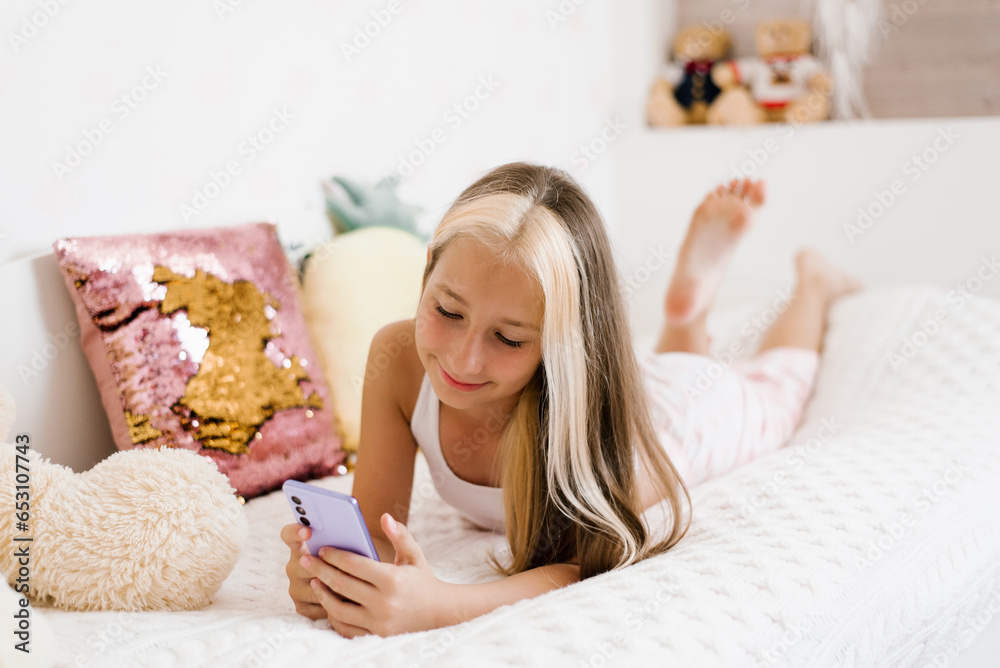 Candid shot of a cute teenage girl in pajamas lying on her stomach on her stomach on the bed posting pictures on social media and checking her friends feed Candid shot of a cute teenage girl in pajamas lying on her stomach on her stomach on the bed posting pictures on social media and checking her friends feed
