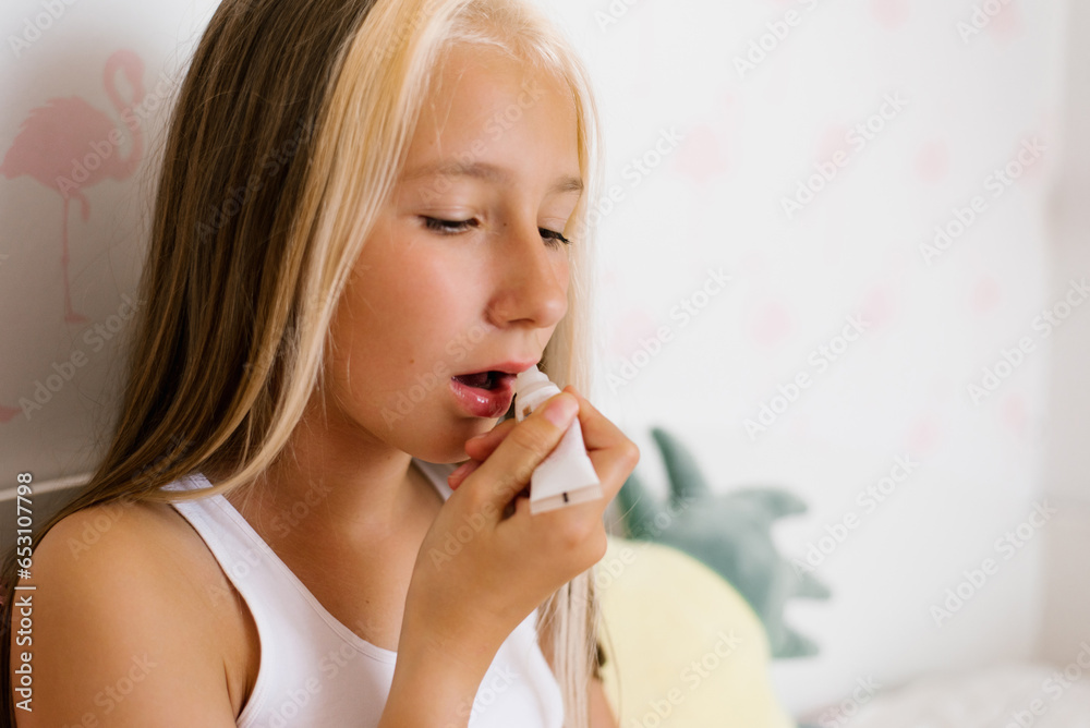 Teenage girl sitting at home on a bed with a cosmetic mirror paints her lips with lip gloss Teenage girl sitting at home on a bed with a cosmetic mirror paints her lips with lip gloss