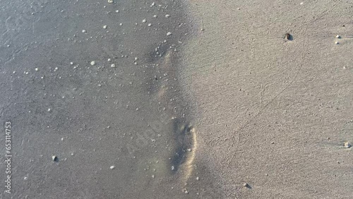 A wave of sea surf washes away the footprints of man on the sand