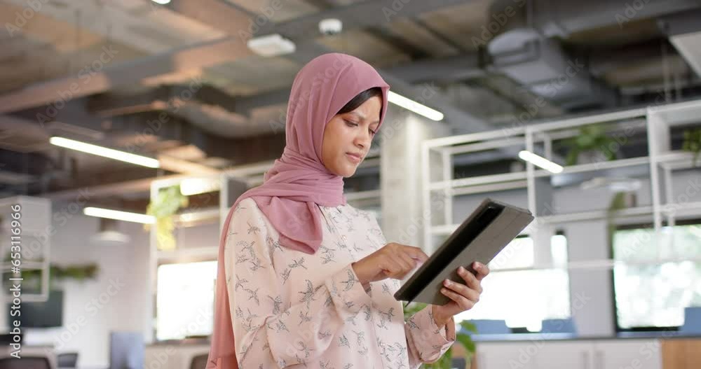 Happy biracial casual businesswoman in hijab using tablet in office, slow motion Happy biracial casual businesswoman in hijab using tablet in office, slow motion