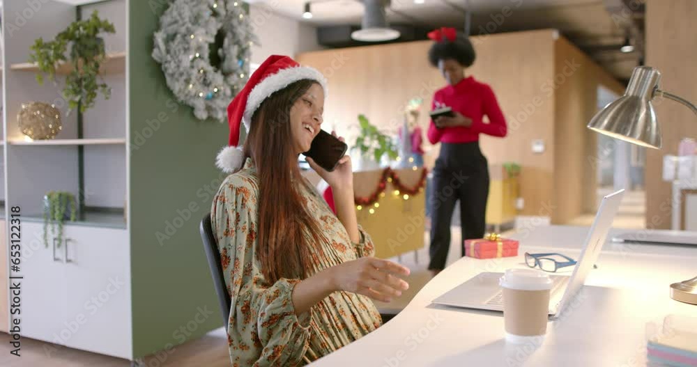 Happy biracial casual businesswoman with christmas hat talking on smartphone in office, slow motion Happy biracial casual businesswoman with christmas hat talking on smartphone in office, slow motion