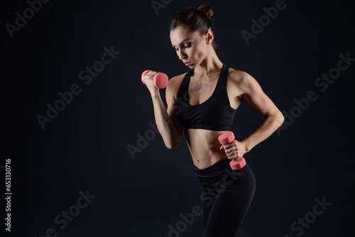 athletic girl in white clothes with dumbbells, on a dark background