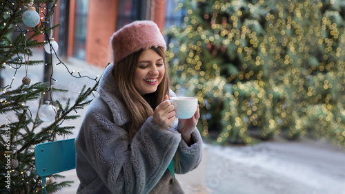 a young woman drinks coffee or tea in a street cafe sitting at a table on Christmas holidays © ulza