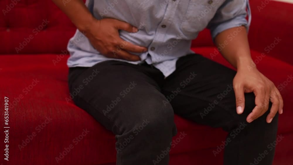 Unhappy man sitting on sofa while holding his stomach, pain in his stomach, suffers from poisoning, spasm, stomach problems. Selective focus. Unhappy man sitting on sofa while holding his stomach, pain in his stomach, suffers from poisoning, spasm, stomach problems. Selective focus.