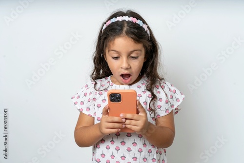 Surprised beautiful kid girl wearing dress using smartphone reading social media news, or important e-mail