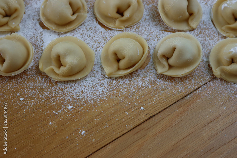 Homemade italian Cappellacci pasta in rows with white flour on wooden table. Similar to tortellini