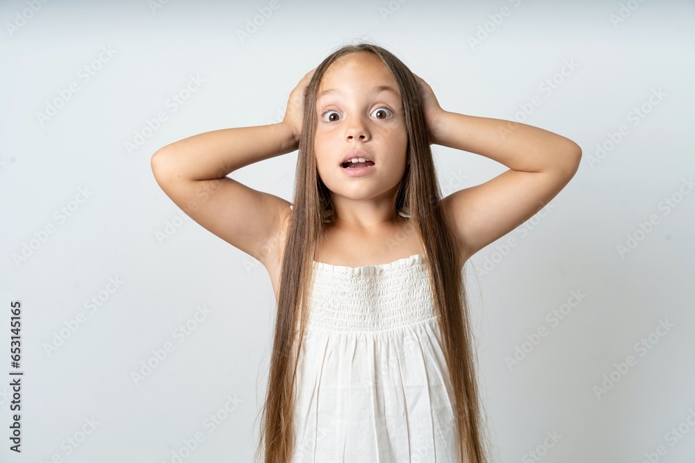 Cheerful overjoyed beautiful kid girl wearing white dress reacts rising hands over head after receiving great news. Cheerful overjoyed beautiful kid girl wearing white dress reacts rising hands over head after receiving great news.