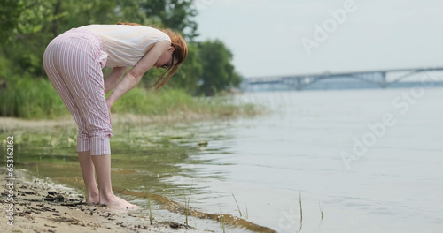 Fotografie Young woman examines living creatures near river bank