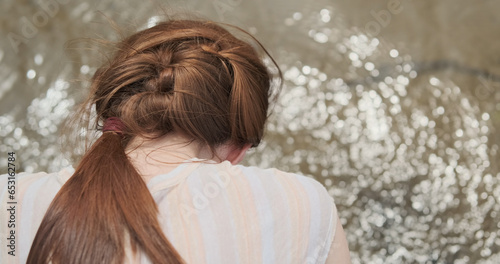 Woman examines the surface of the river water, close-up, rear view. Reflection of the sun in the waves of the river.