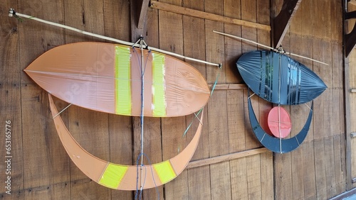 Wau bulan or moon kite hanging on a wooden wall as decoration. Traditional kites with shiny plain motifs. Wau bulan got its name from the crescent moon-like shape of its lower section.