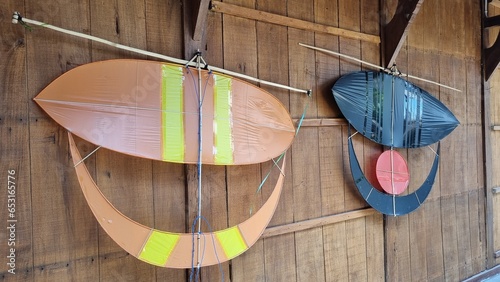 Wau bulan or moon kite hanging on a wooden wall as decoration. Traditional kites with shiny plain motifs. Wau bulan got its name from the crescent moon-like shape of its lower section. photo