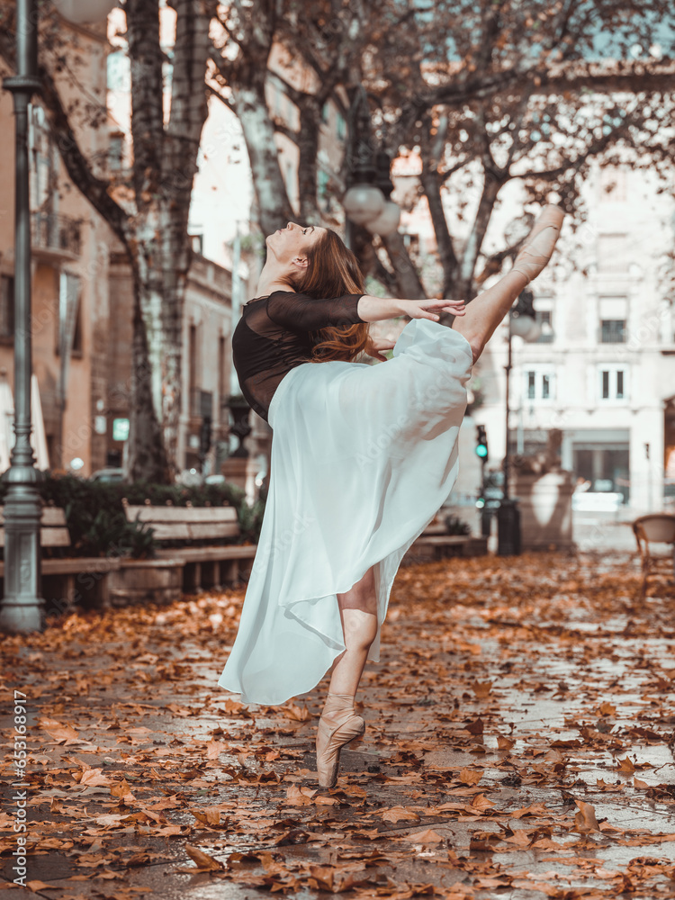 Ballerina in white skirt performing split in autumn street