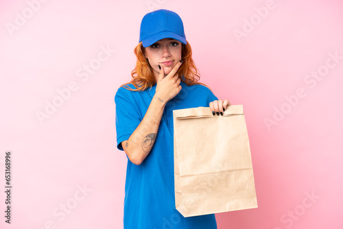 Young caucasian woman taking a bag of takeaway food isolated on pink background thinking