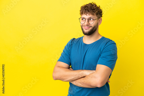 Young handsome caucasian man isolated on yellow background making doubts gesture while lifting the shoulders