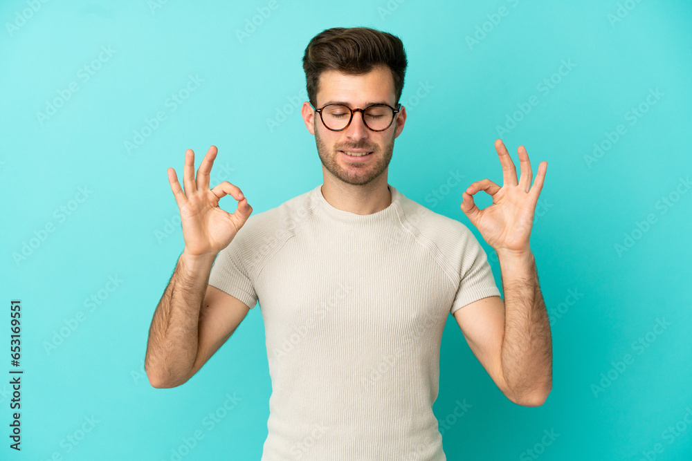 Young caucasian handsome man isolated on blue background in zen pose