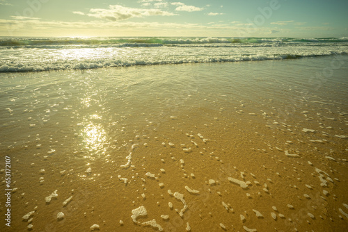 Pastel colors as surf waves break and roll across sandy beach with the sun glistening in the shallow foamy water. Early morning at Kawana, Sunshine Coast, Queensland tourist destination.  photo