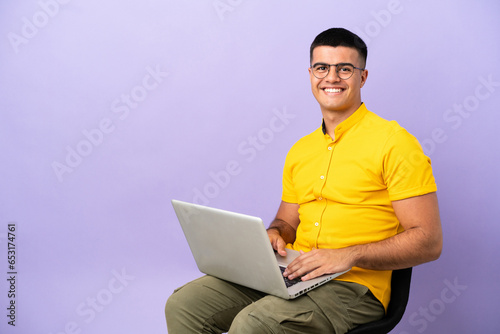 Young man sitting on a chair with laptop laughing