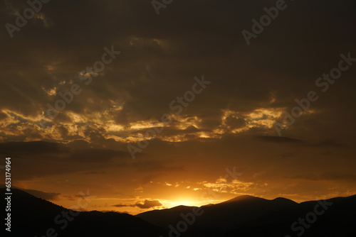 Sunset above horizon line with sun setting down behind Caucasian mountains and sun rays. Panoramic view form mountains peak on the bright sunset with clouds.