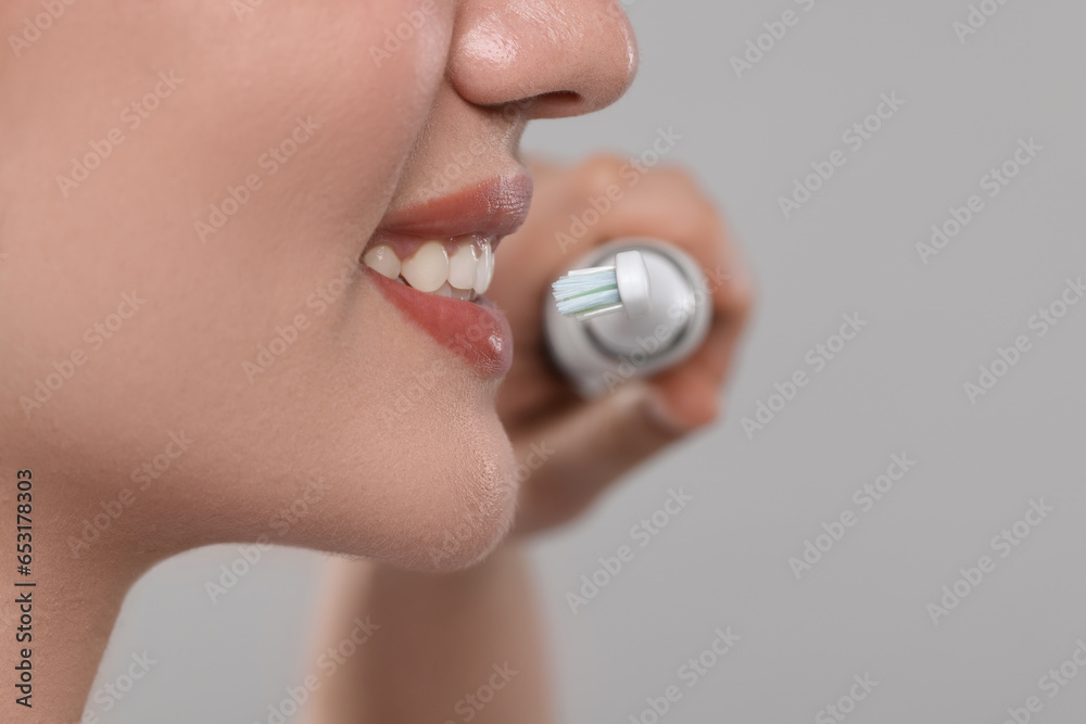 Fototapeta premium Woman brushing her teeth with electric toothbrush on light grey background, closeup. Space for text