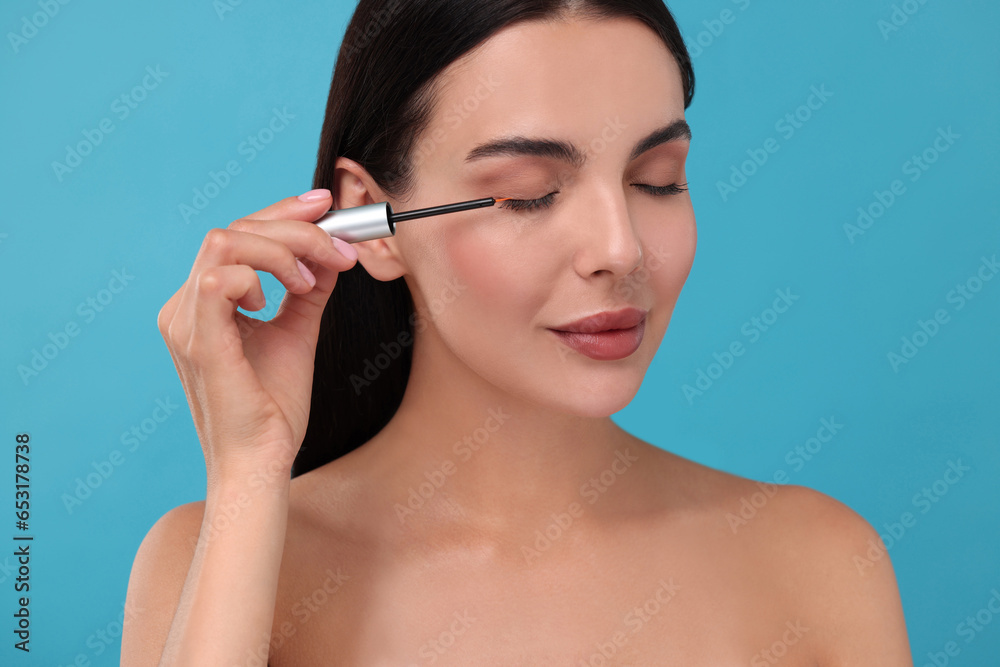 Beautiful woman applying serum onto her eyelashes on light blue background. Cosmetic product Beautiful woman applying serum onto her eyelashes on light blue background. Cosmetic product