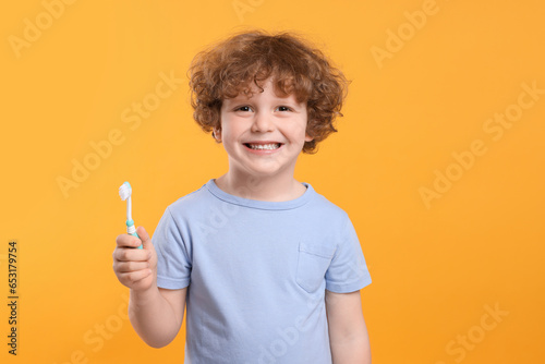Cute little boy holding plastic toothbrush on yellow background