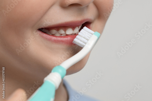 Cute little boy brushing his teeth with plastic toothbrush on light grey background, closeup. Space for text