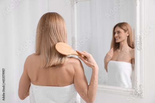 Woman after shower brushing her hair near mirror in room